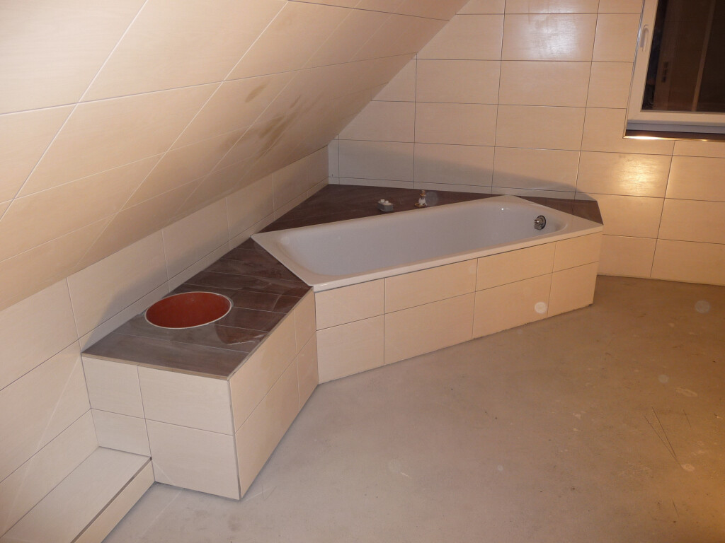Bathroom with built-in bathtub under a sloping ceiling, dark stone surface, and a red round pot.