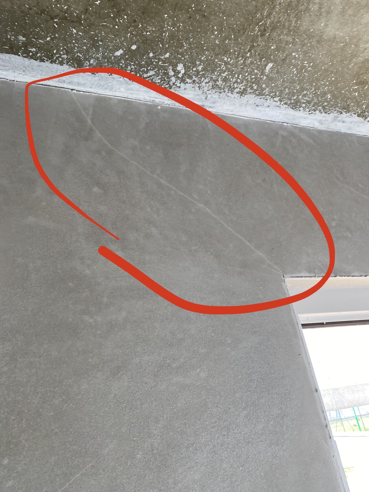 Gray interior wall near the ceiling with fine crack trace; red marking highlights the crack.
