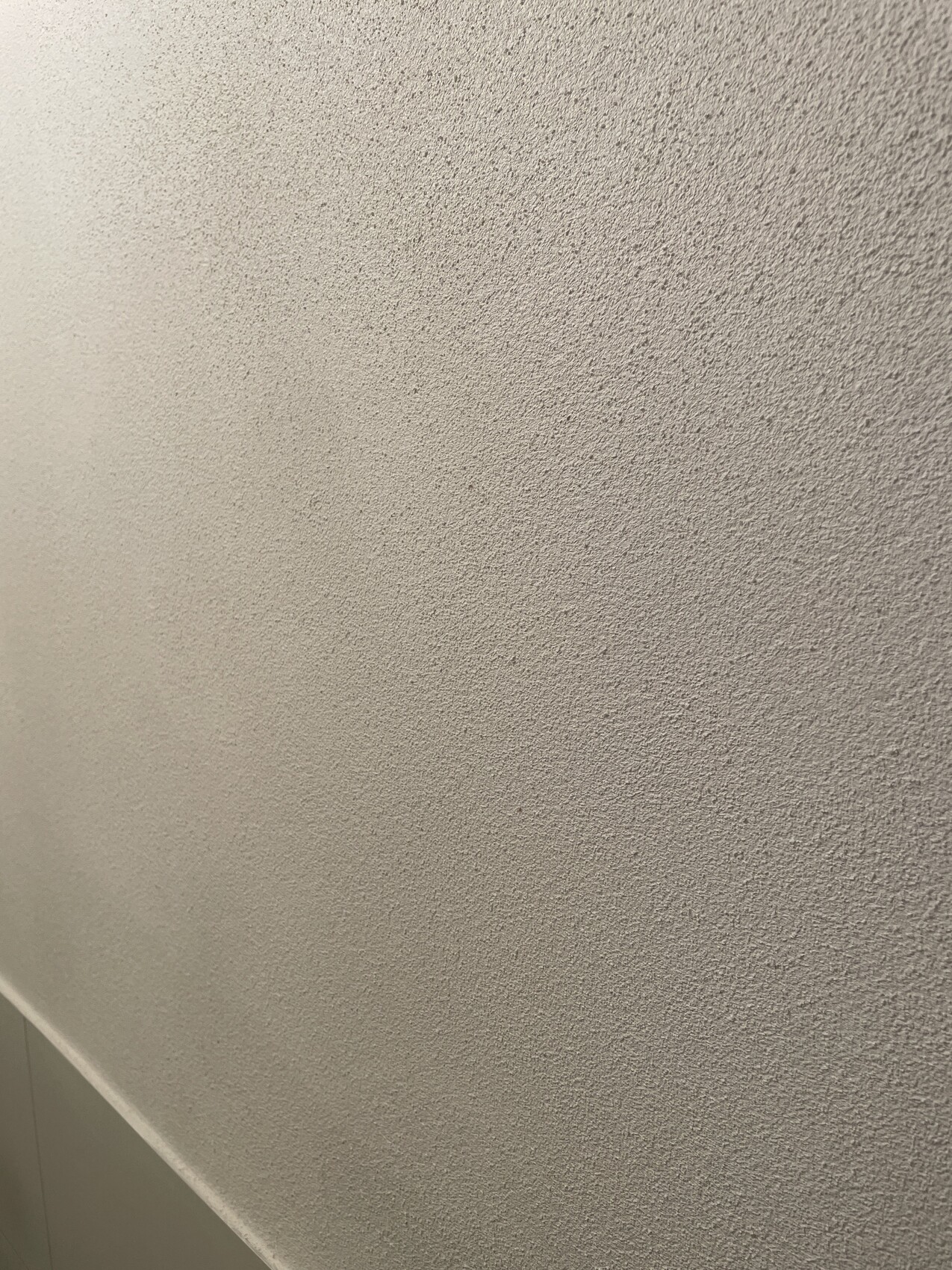 Close-up of a light gray, textured plaster wall with a corner at the bottom left.