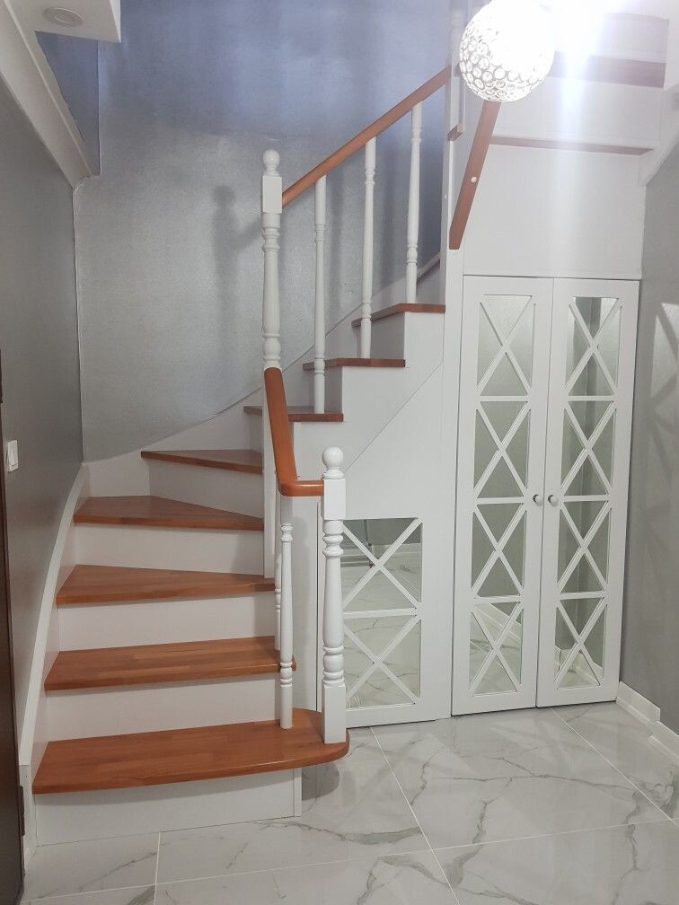 White staircase with brown wooden steps and railing; underneath, a glass cabinet with cross-grid panels.