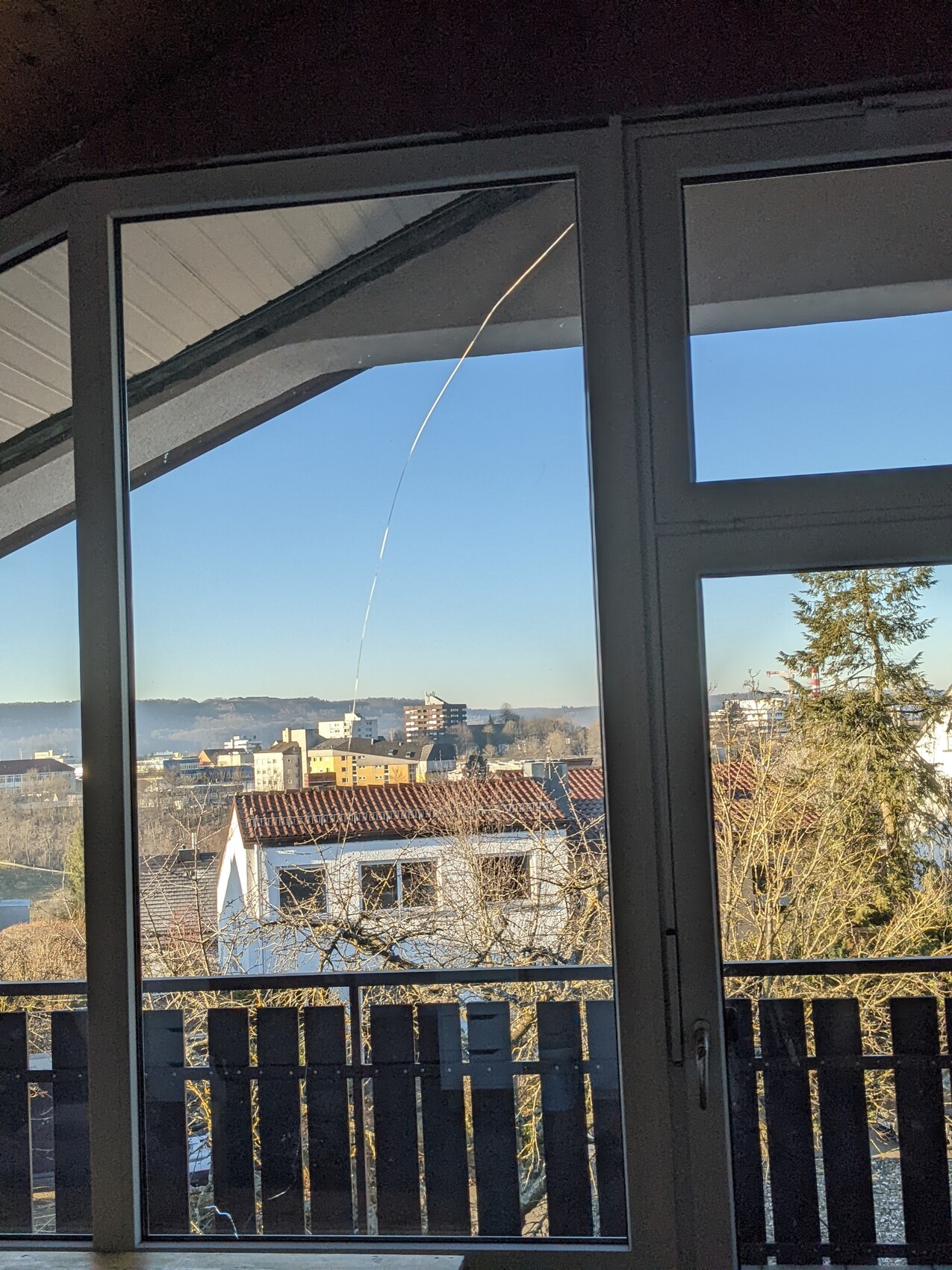 View through window onto suburb: red roofs, bare trees, blue sky; bright arc in the sky.