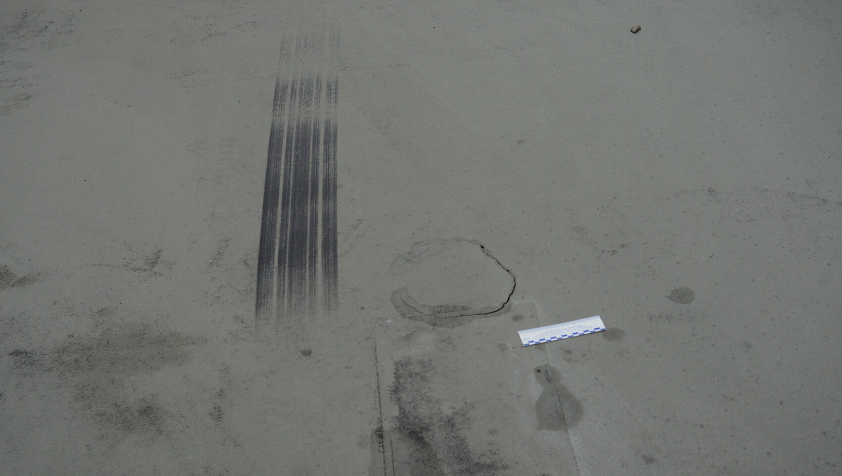 Concrete floor with long vertical tire marks, circular crack, and measuring strip.