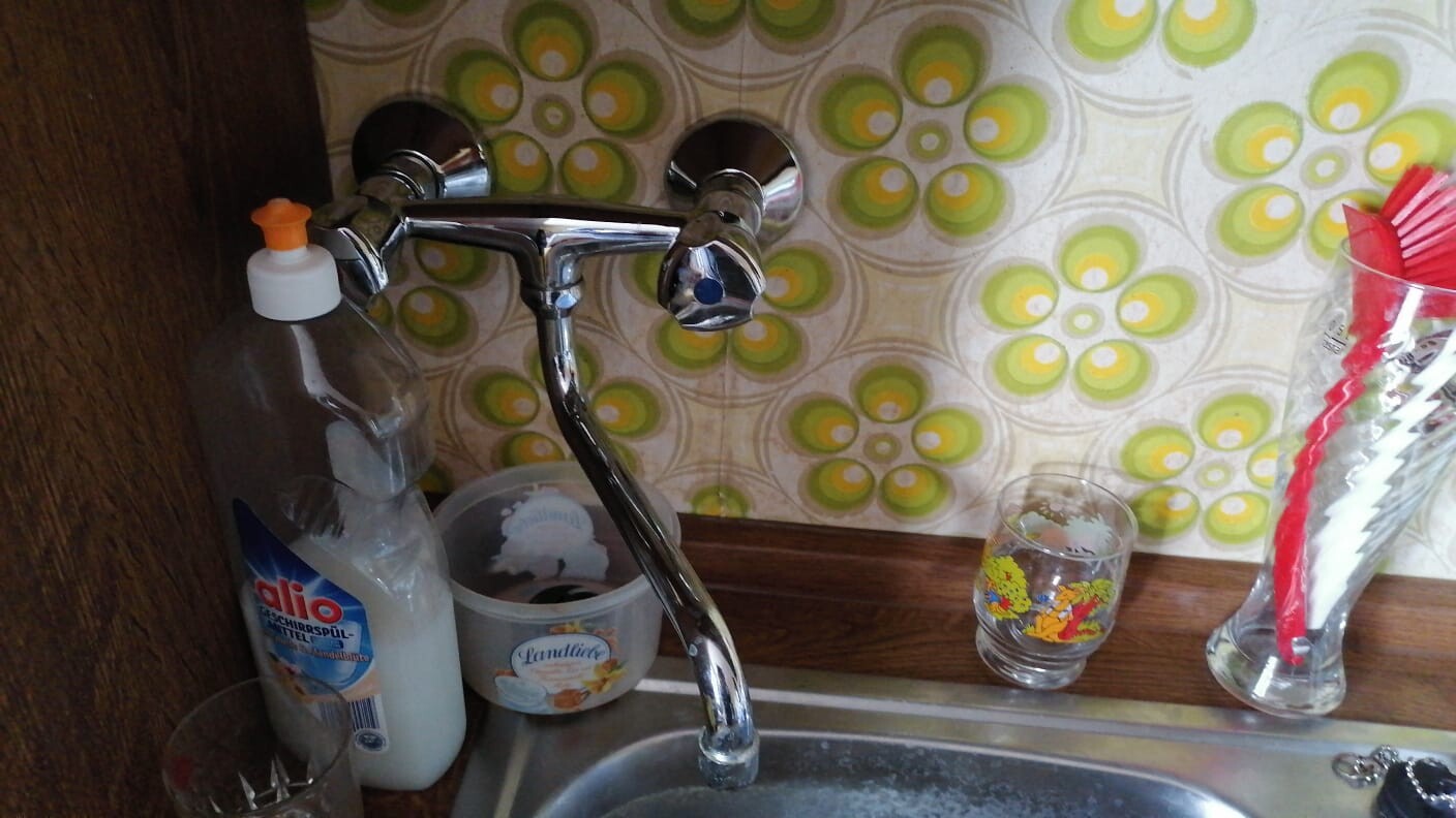 Sink with chrome tap; dish soap on the left, container, glass with colorful design, glass with red straws