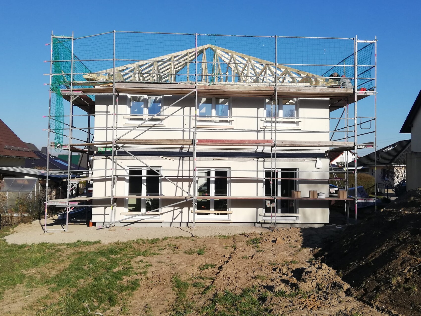 Two-story house under scaffolding with visible roof structure and outdoor construction work