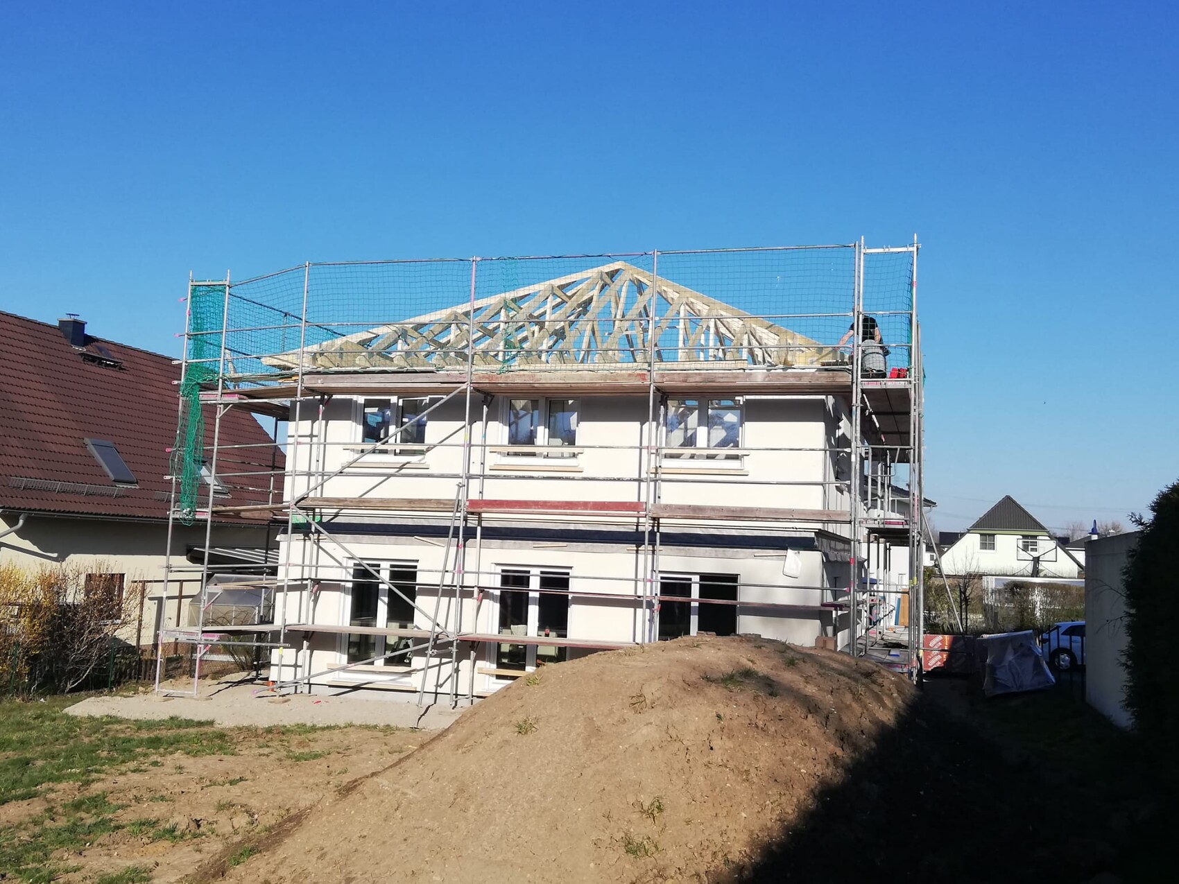 Two-story house with scaffolding; roof frame is being constructed, blue sky in the background