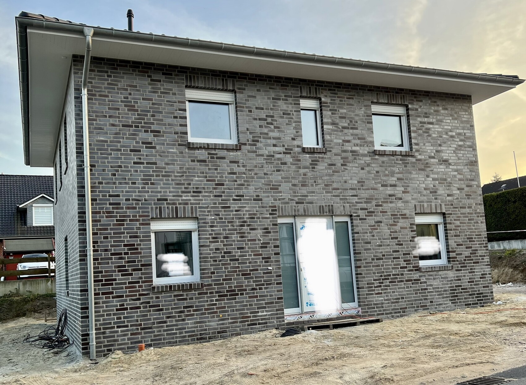 Two-story, dark gray brick house under construction with window fronts and construction site in front
