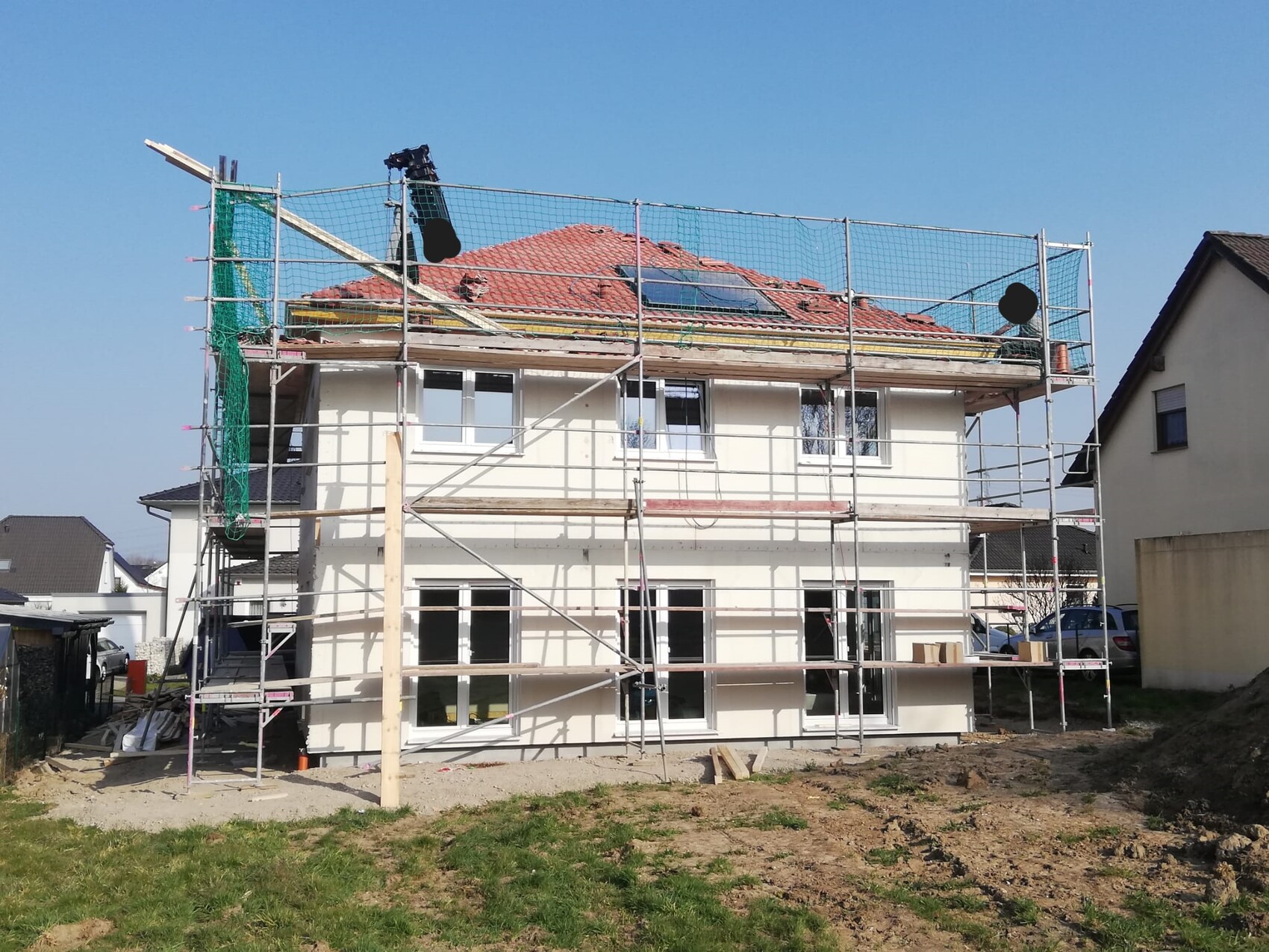 Two-story house under construction with scaffolding, red tiled roof and open windows.
