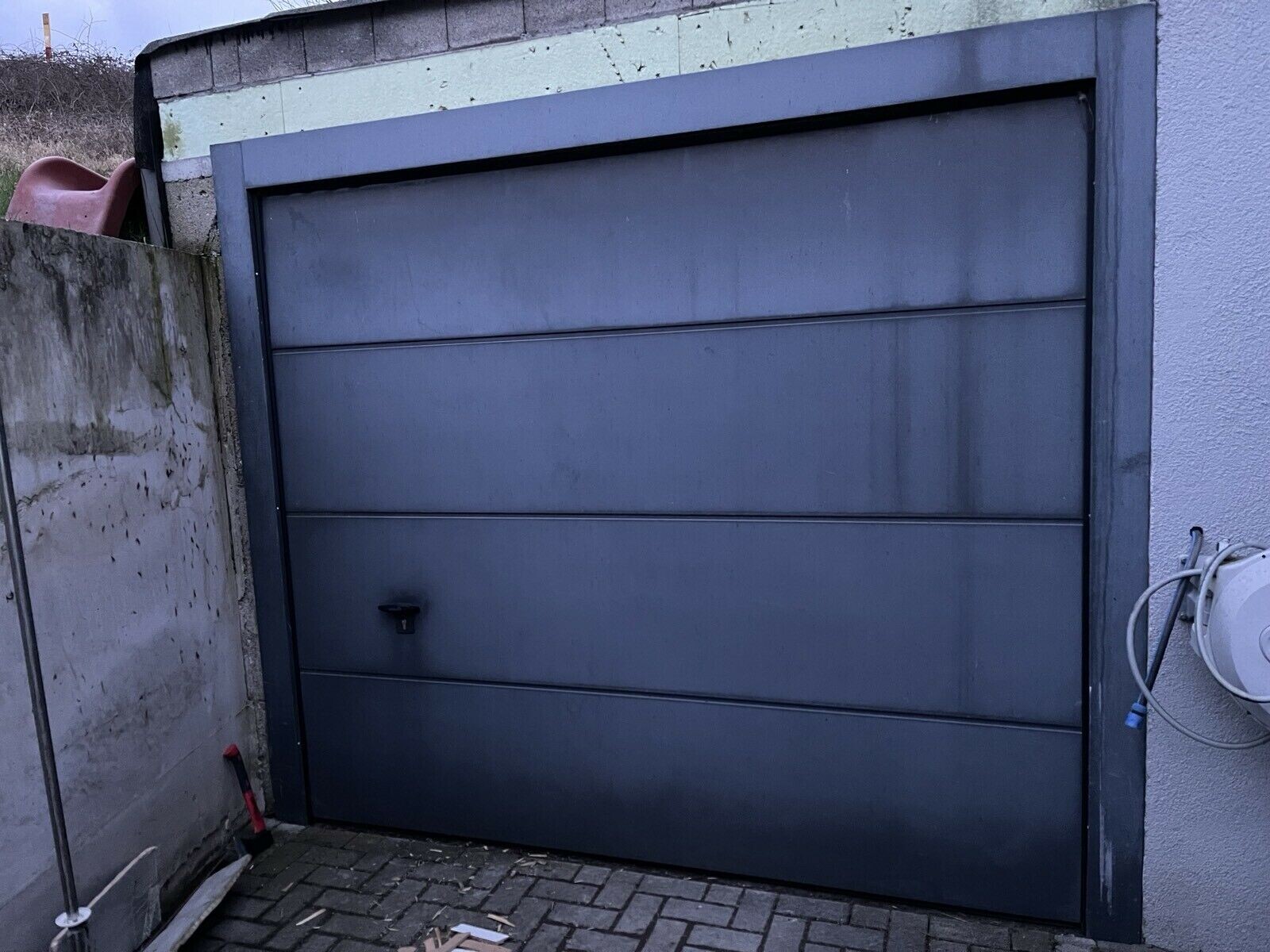 Large gray metal garage door with horizontal panels in front of an exterior wall.