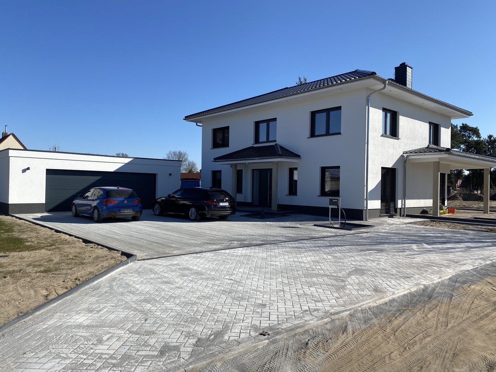 Modern white detached house with garage on the left, two cars on a paved driveway.