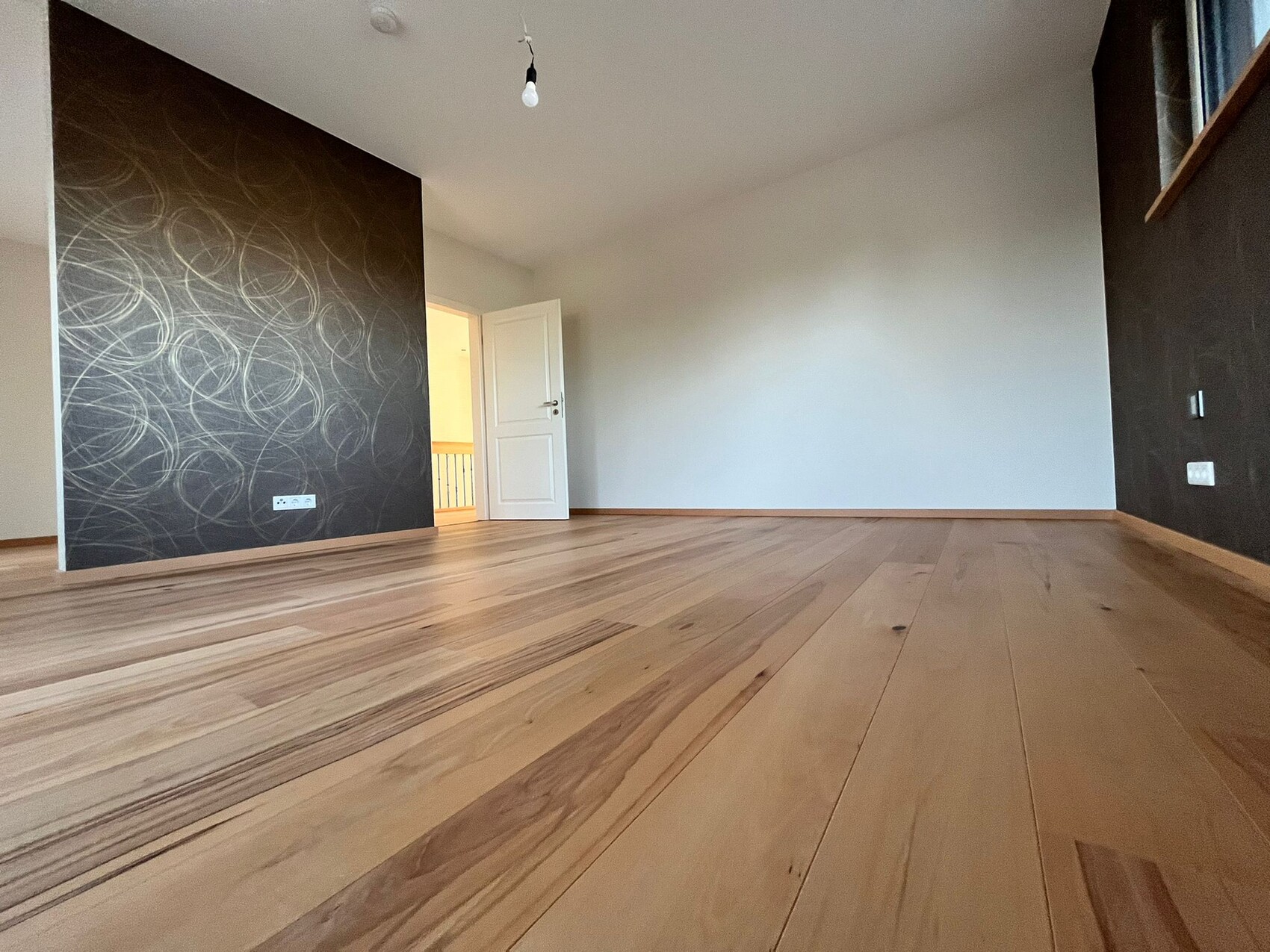 Empty room with wooden floor, left dark wall with spiral pattern, open door to the hallway.