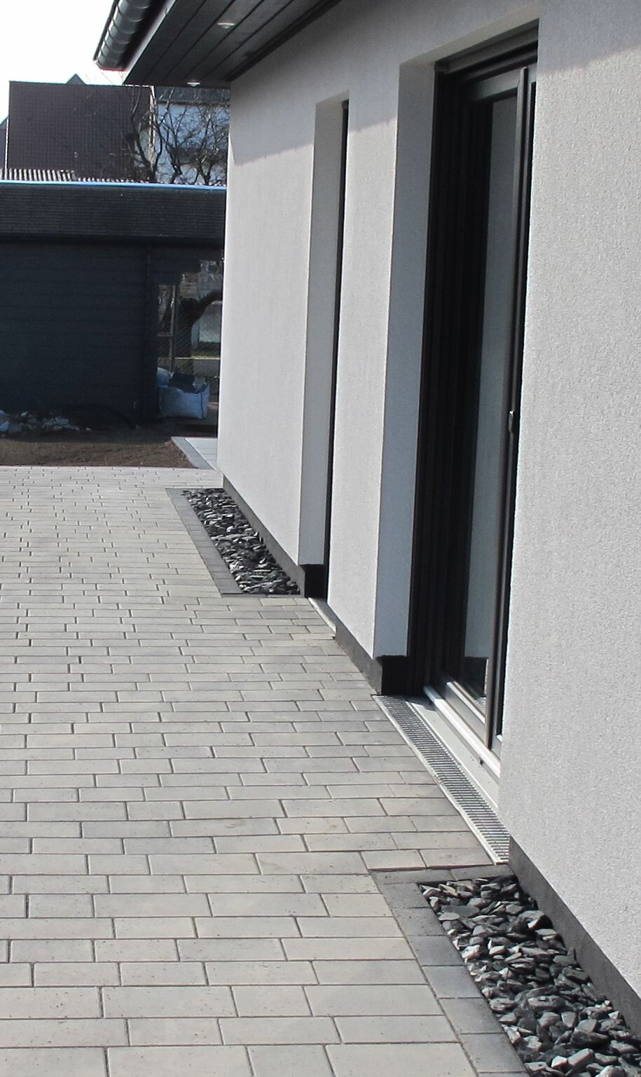 Modern white facade with large glass sliding doors, paved forecourt, and gravel strip.