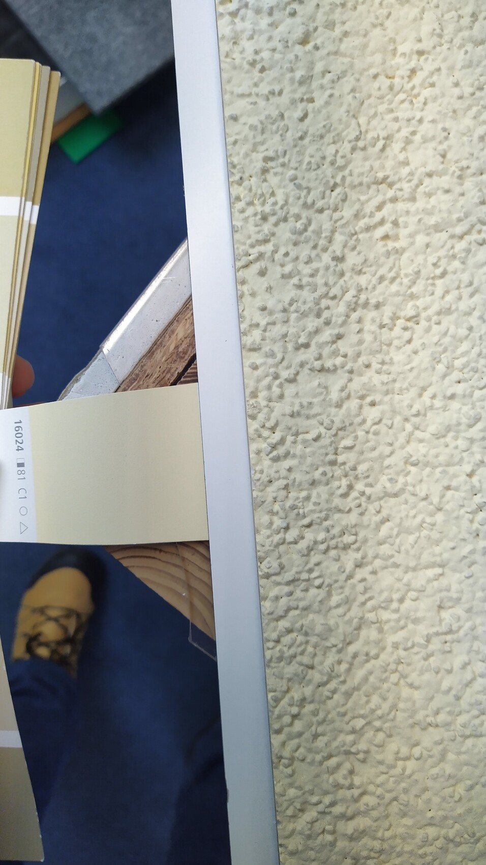 Beige Farbkarte wird von einer Person gehalten, neben rauer Wand und blauem Boden.