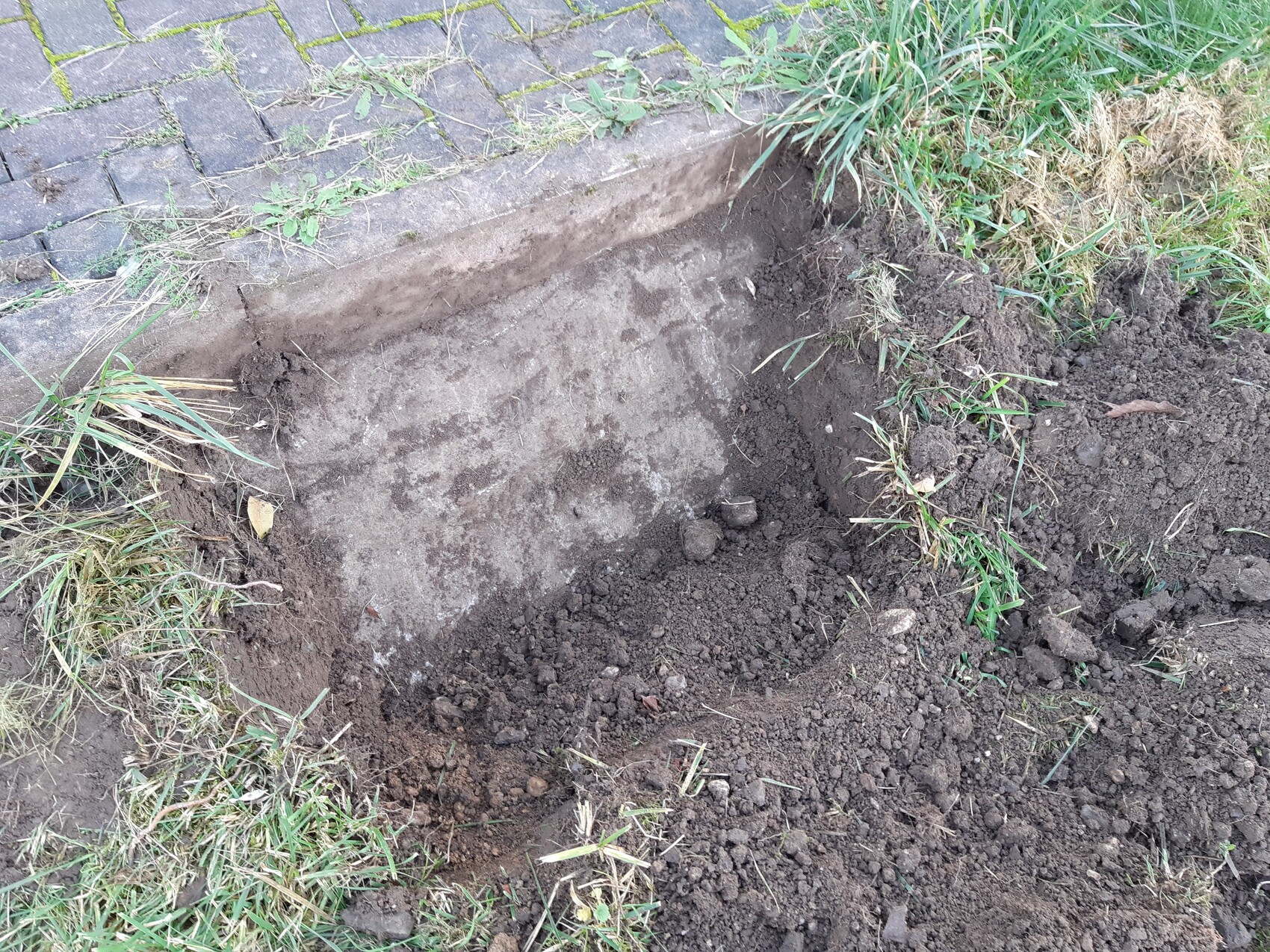 Excavated ground and foundation area next to paved walkway with grass