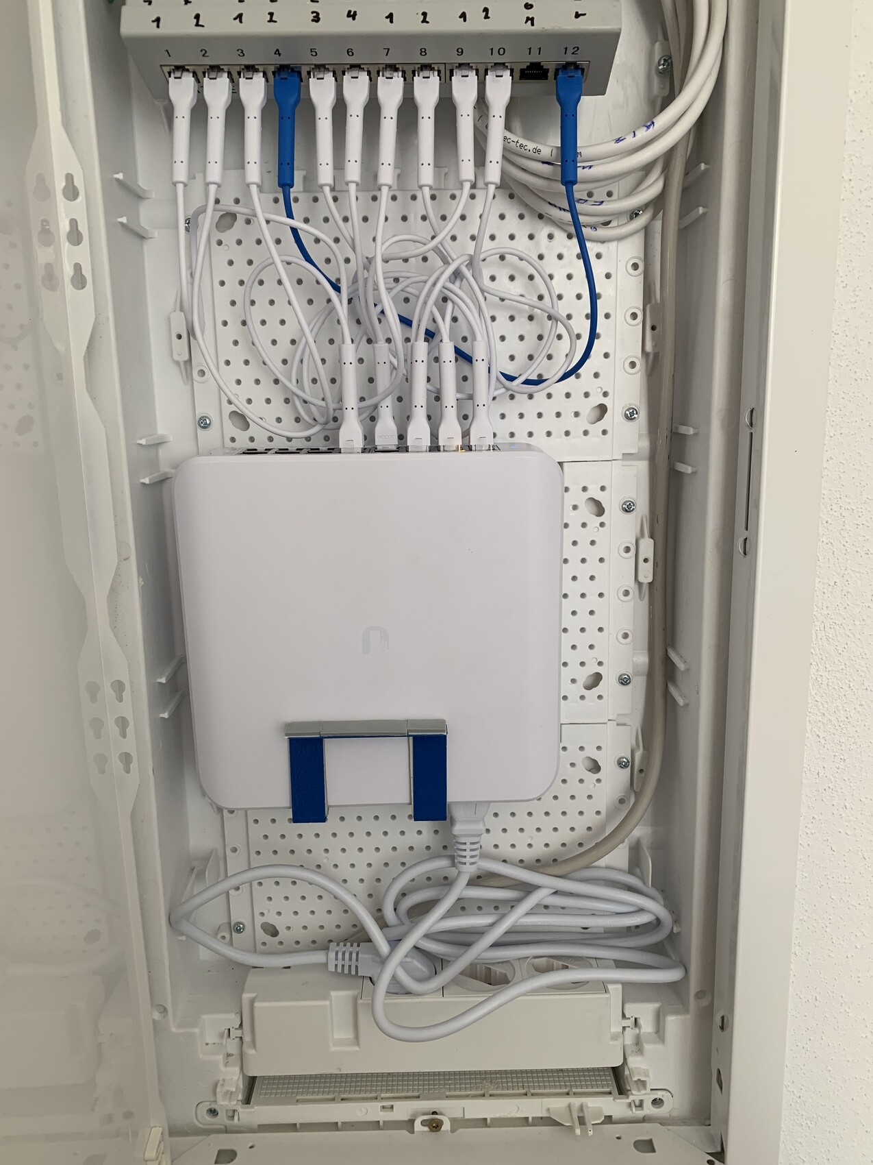 Network cabinet: patch panel with many white cables, two blue cables, white box below