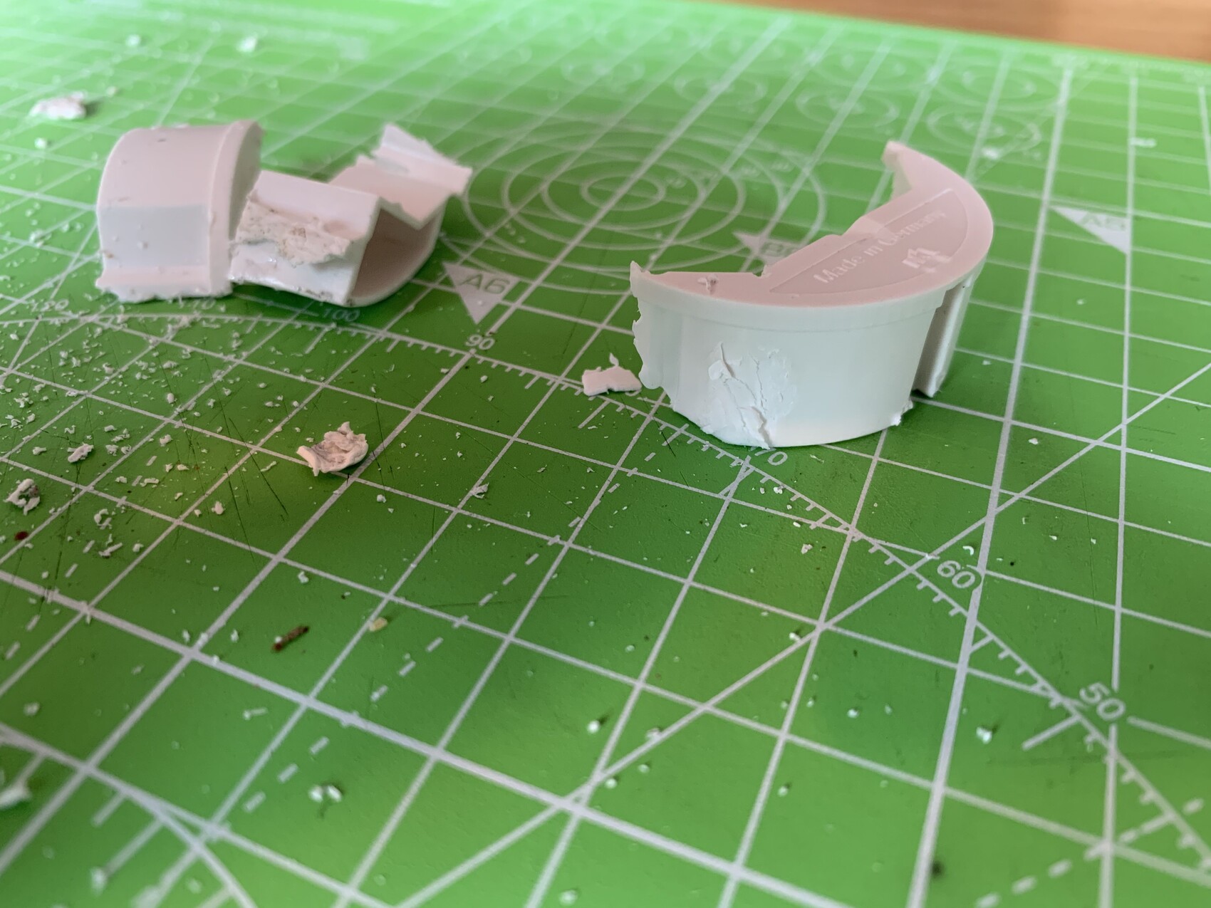 Broken white plastic parts and fragments on green cutting mat (model making).