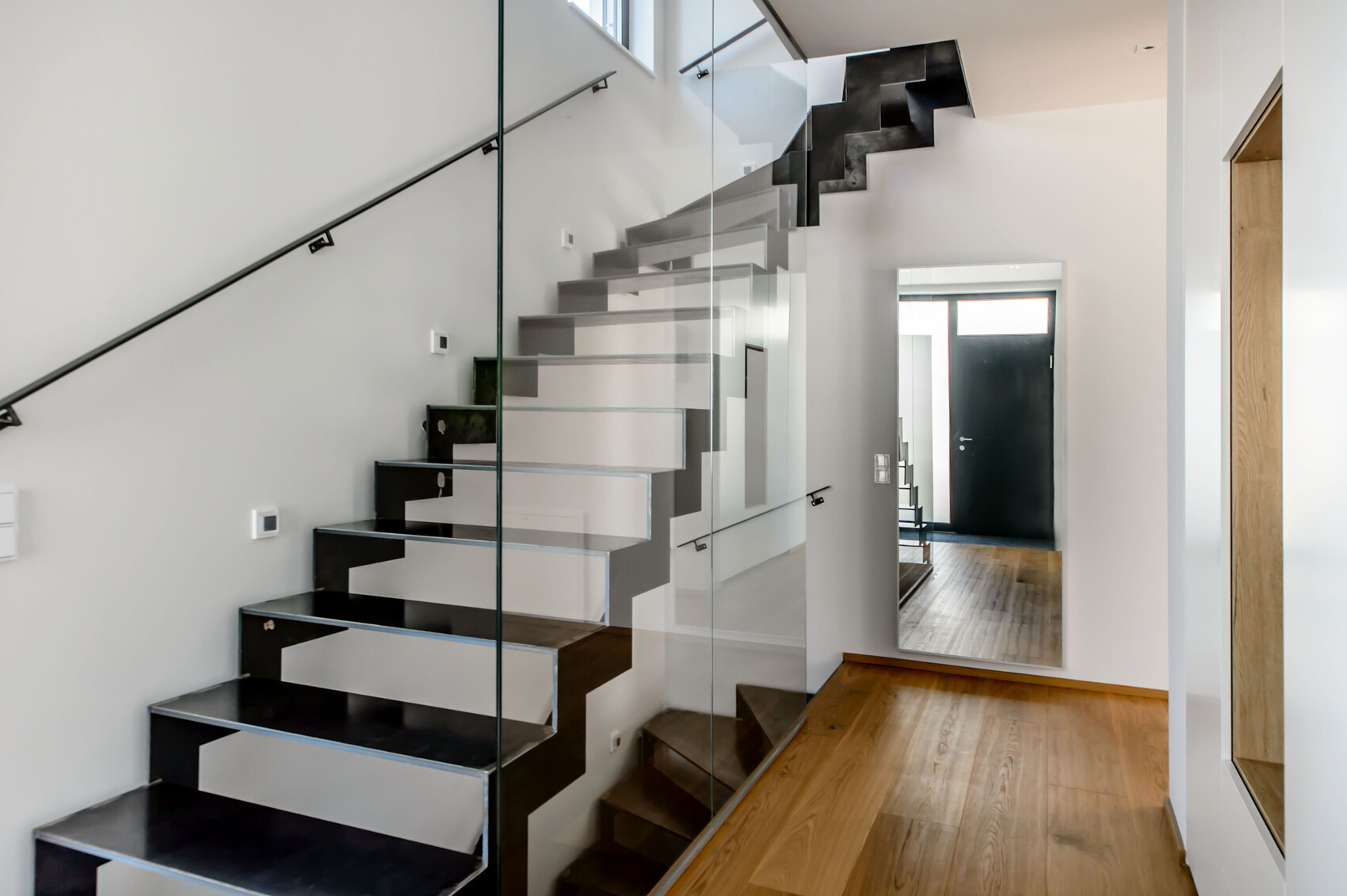 Modern staircase with glass railing and open space; bright interior, wooden floor.