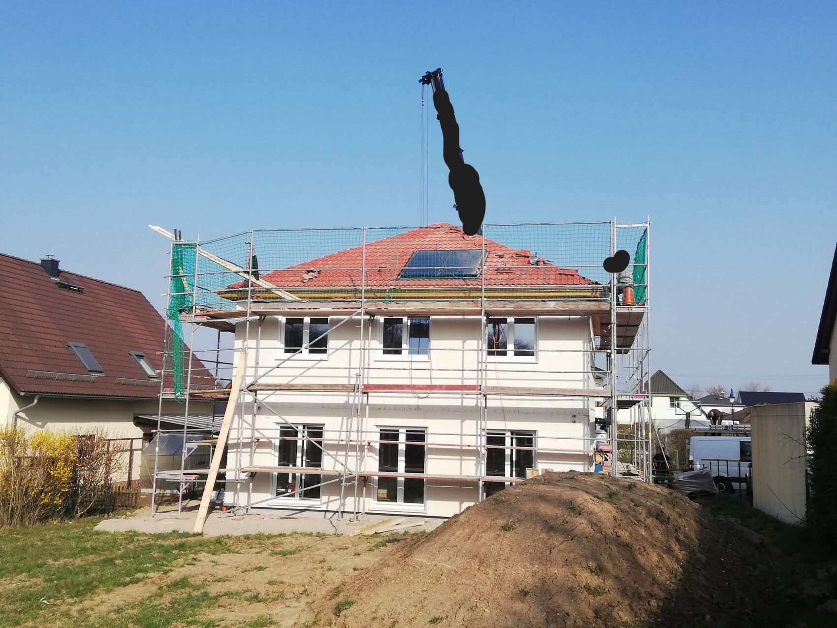 Two-story house with scaffolding and crane, earthworks in front of the building.