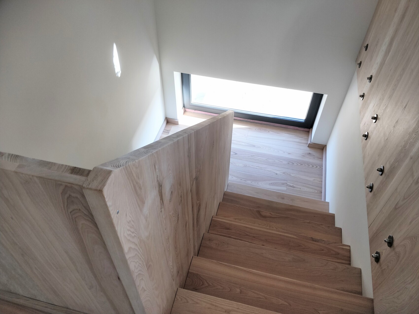 Bright wood staircase from above: steps, wood paneling on the wall, window at the bottom