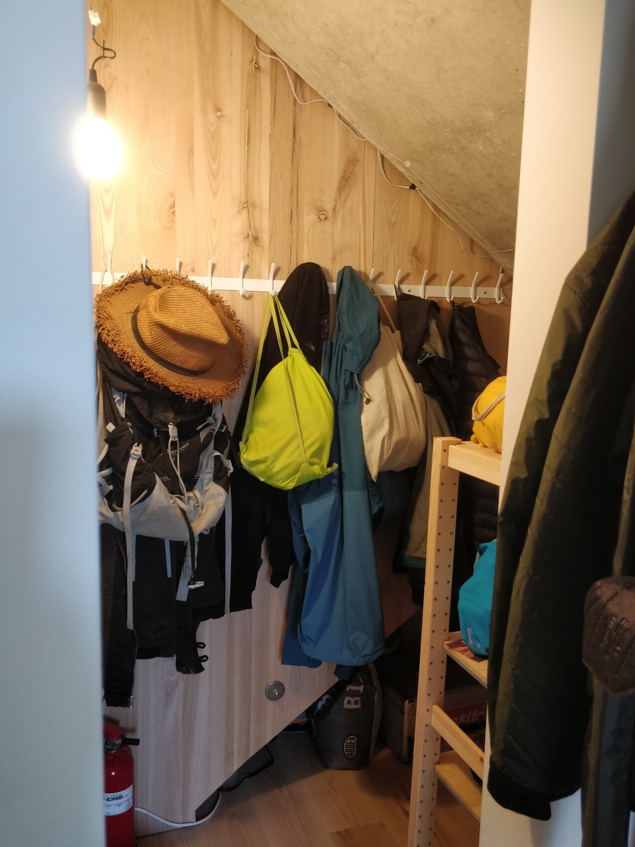 Small cloakroom with coat rack, jackets, neon green backpack, hat, light bulb.