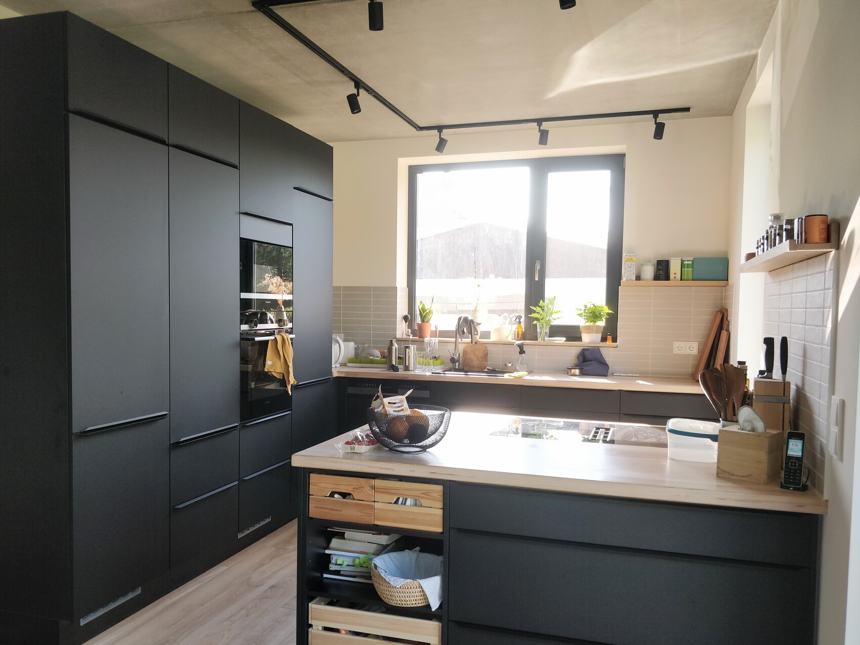Modern kitchen with black fronts, cooking island, and windowsill with plants.