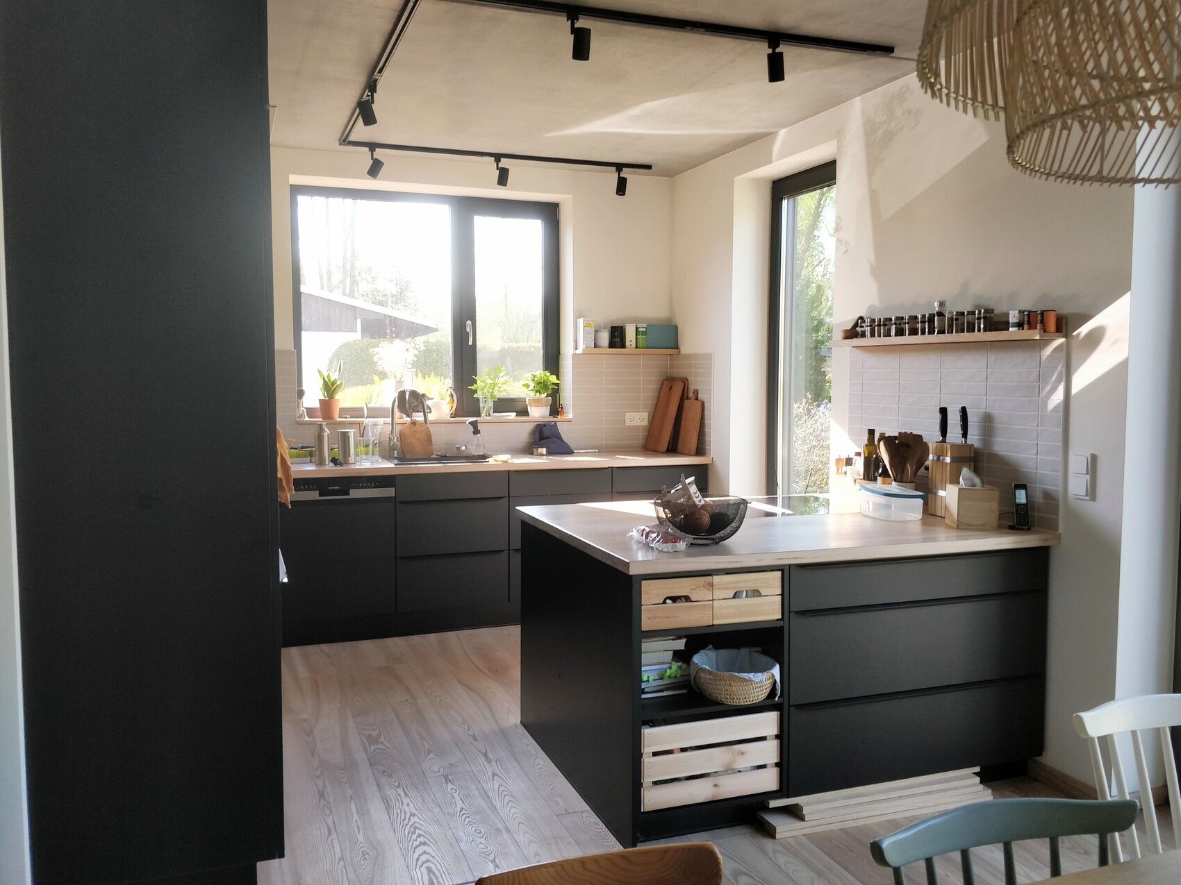 Modern kitchen with dark island, two large windows, kitchen utensils, and plants.