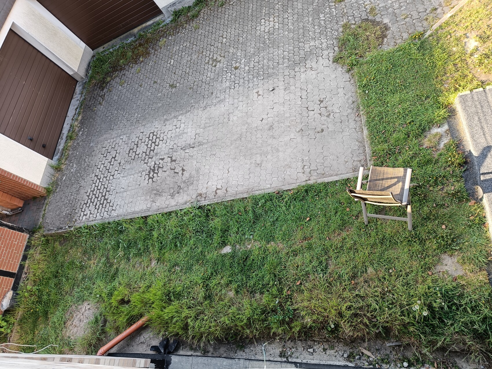 Ein umgestellter Gartenstuhl liegt auf dem Gras neben einer gepflasterten Einfahrt.