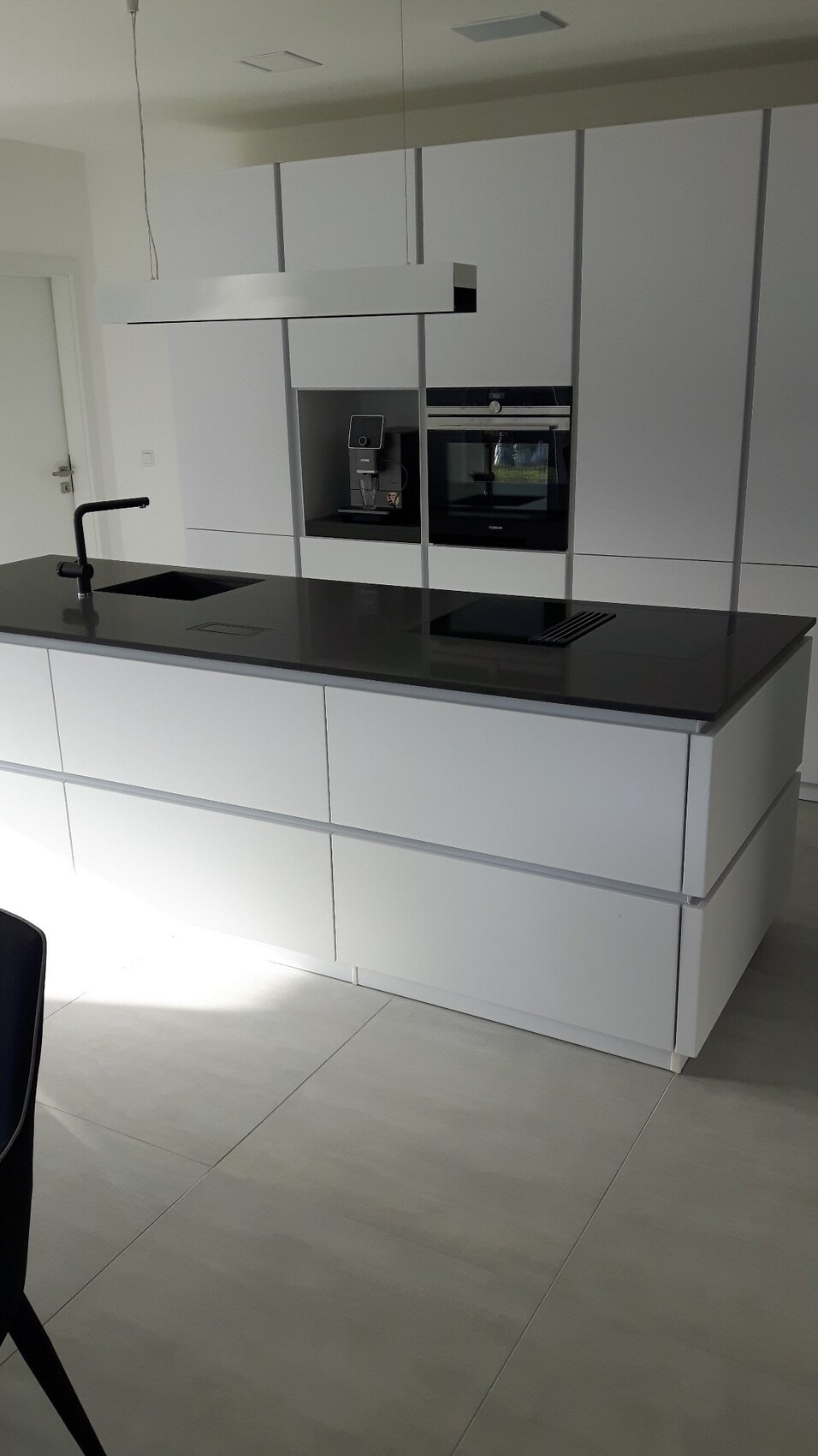 Moderne weiße Küche mit Insel, schwarze Arbeitsplatte, Spüle, Induktionskochfeld und Ofen.