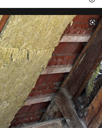 Roof structure with yellow insulation between wooden beams and brick wall