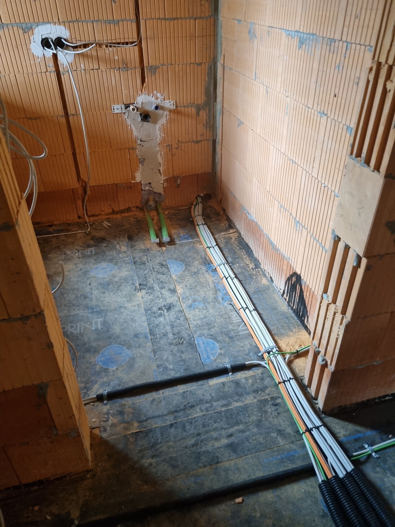 Construction site: exposed pipes, cable bundles on the floor, brick walls.