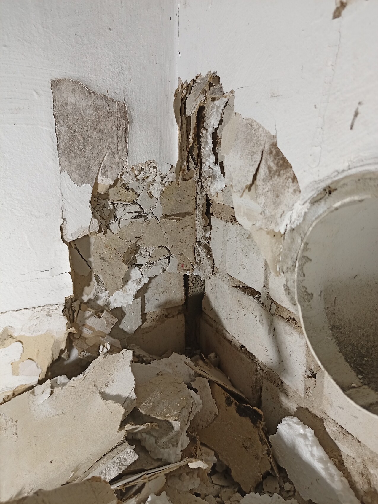Corner of a plastered wall with crumbling plaster; right edge showing round mirror frame