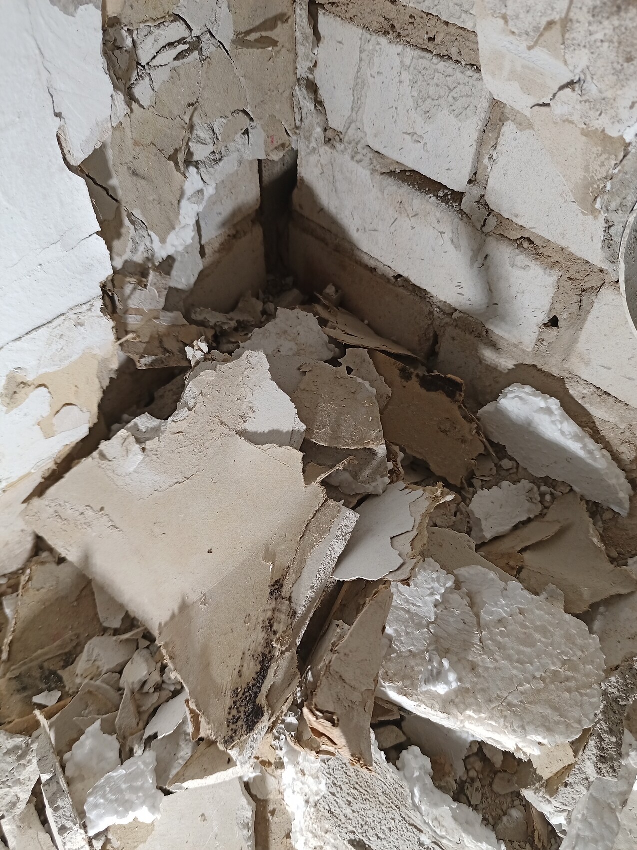 Crumbled plaster and brick wall with debris in a corner