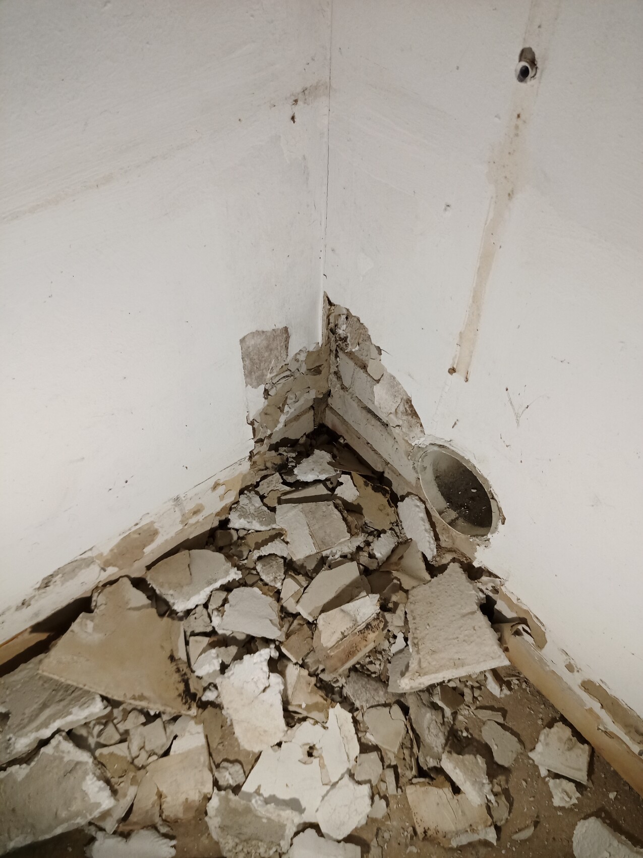 Corner of a room with broken plaster and plaster debris on the floor
