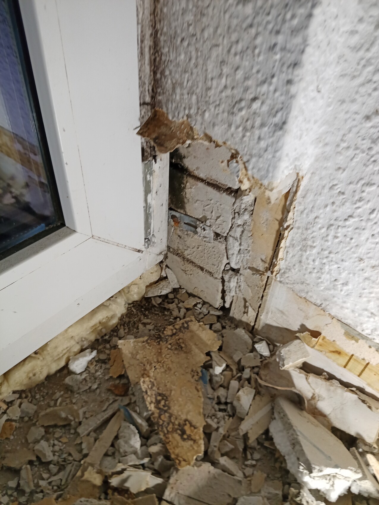 Damaged exterior wall at window: flaking plaster, exposed masonry and debris