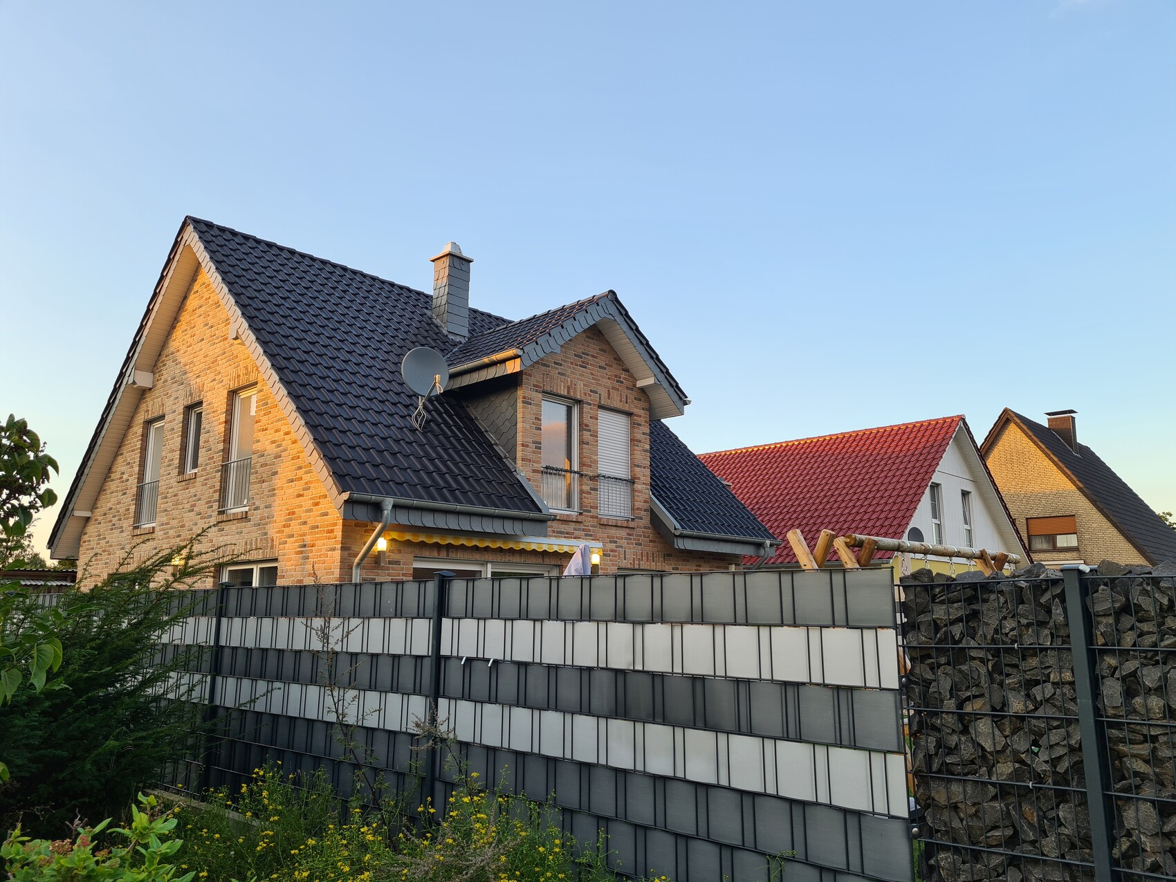 Two-story houses with blue and red tiled roofs, satellite dish, fence and garden plants.