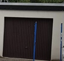 Brown garage door in front of cream-colored wall, blue supports in the foreground.