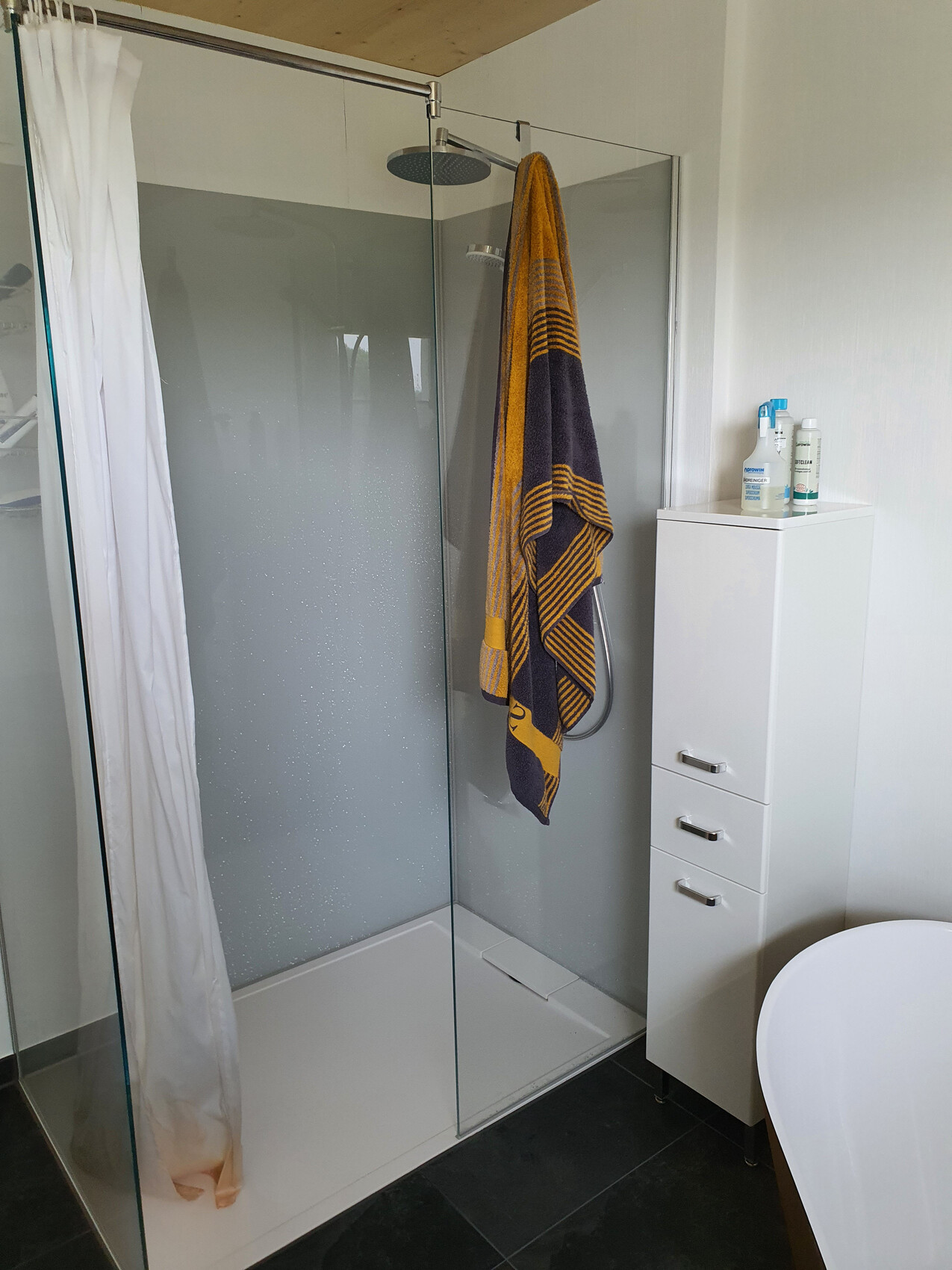 Bathroom with glass shower, yellow-dark blue striped towel, white cabinet with three drawers.