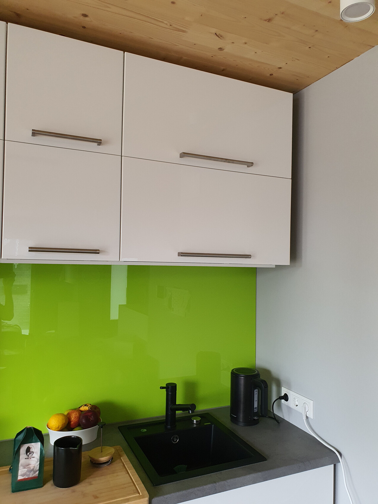 Modern kitchen with white upper cabinet, green glass backsplash, black sink and kettle.