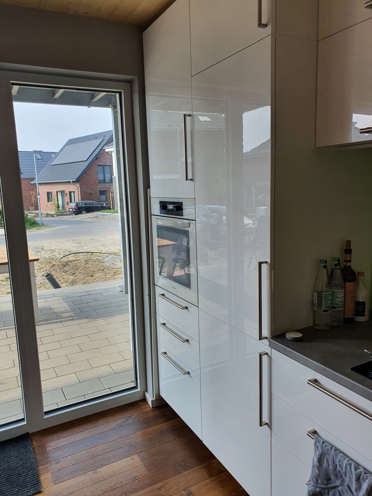 Modern kitchen with white high-gloss cabinets and oven; glass door to the outside