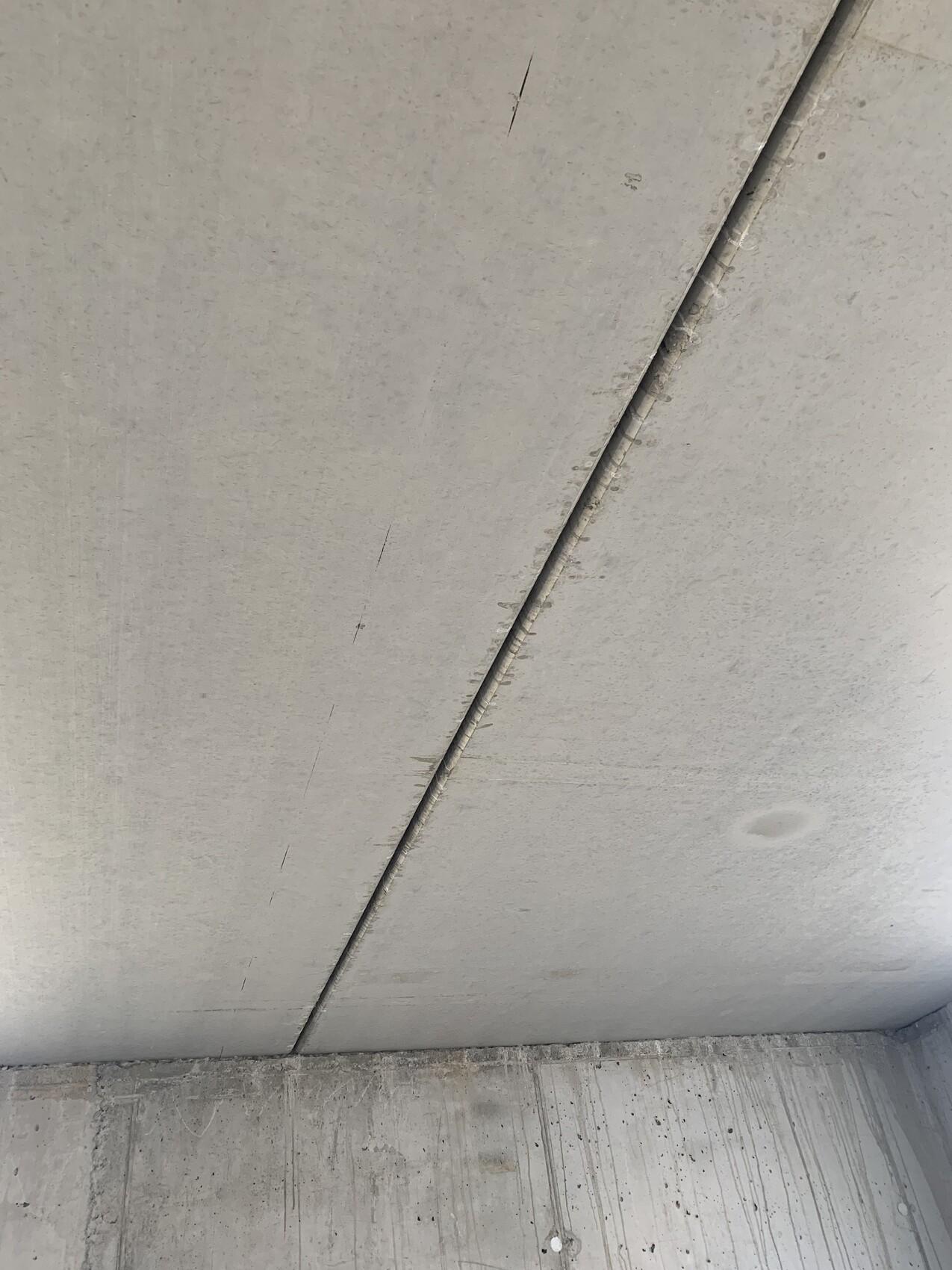 Raw concrete ceiling with diagonal joint, rough surface, concrete floor visible.