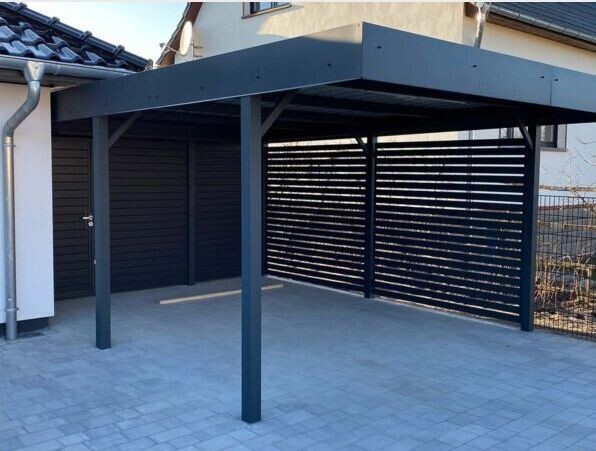 Moderne dunkle Carport-Überdachung aus Metall mit Flachdach und Lamellenwand auf gepflastertem Hof