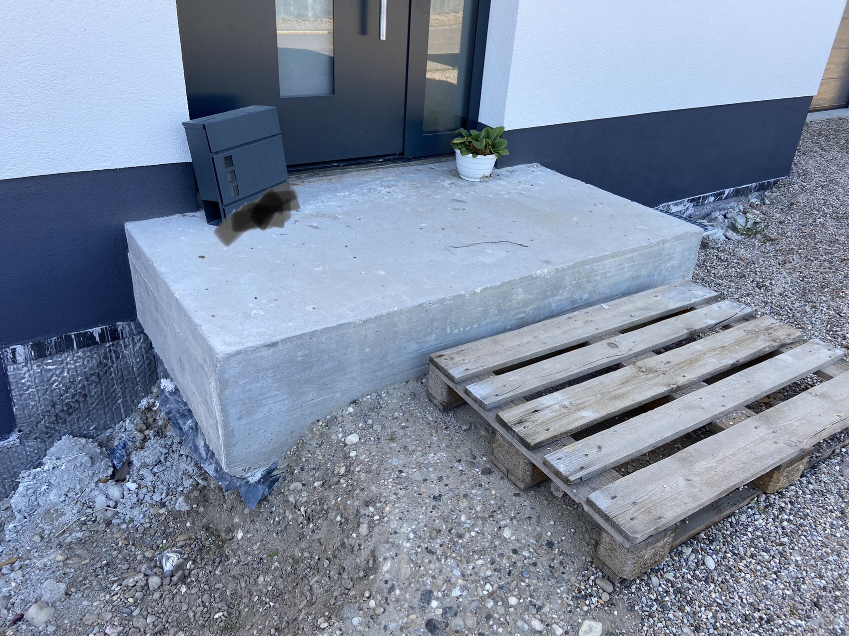 Outdoor area: concrete step in front of a dark front door, mailbox, plant, and wooden pallet