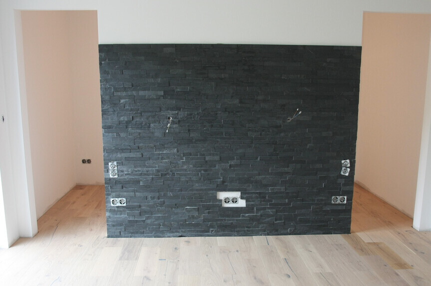 Partition wall made of dark stone slabs with power outlets and cable outlets in a light room.