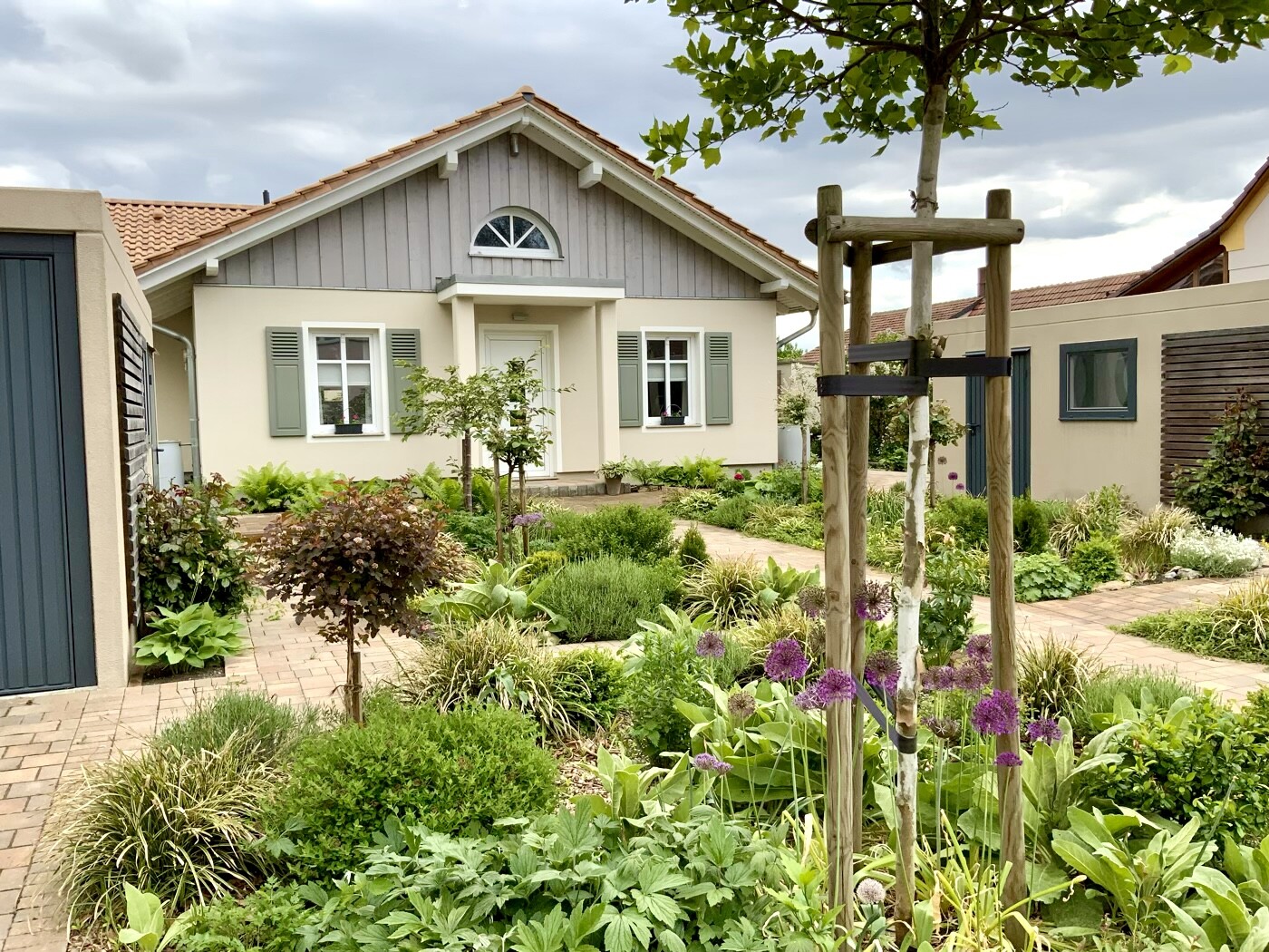 Small detached house with paved garden path, perennial flower bed and allium flowers.