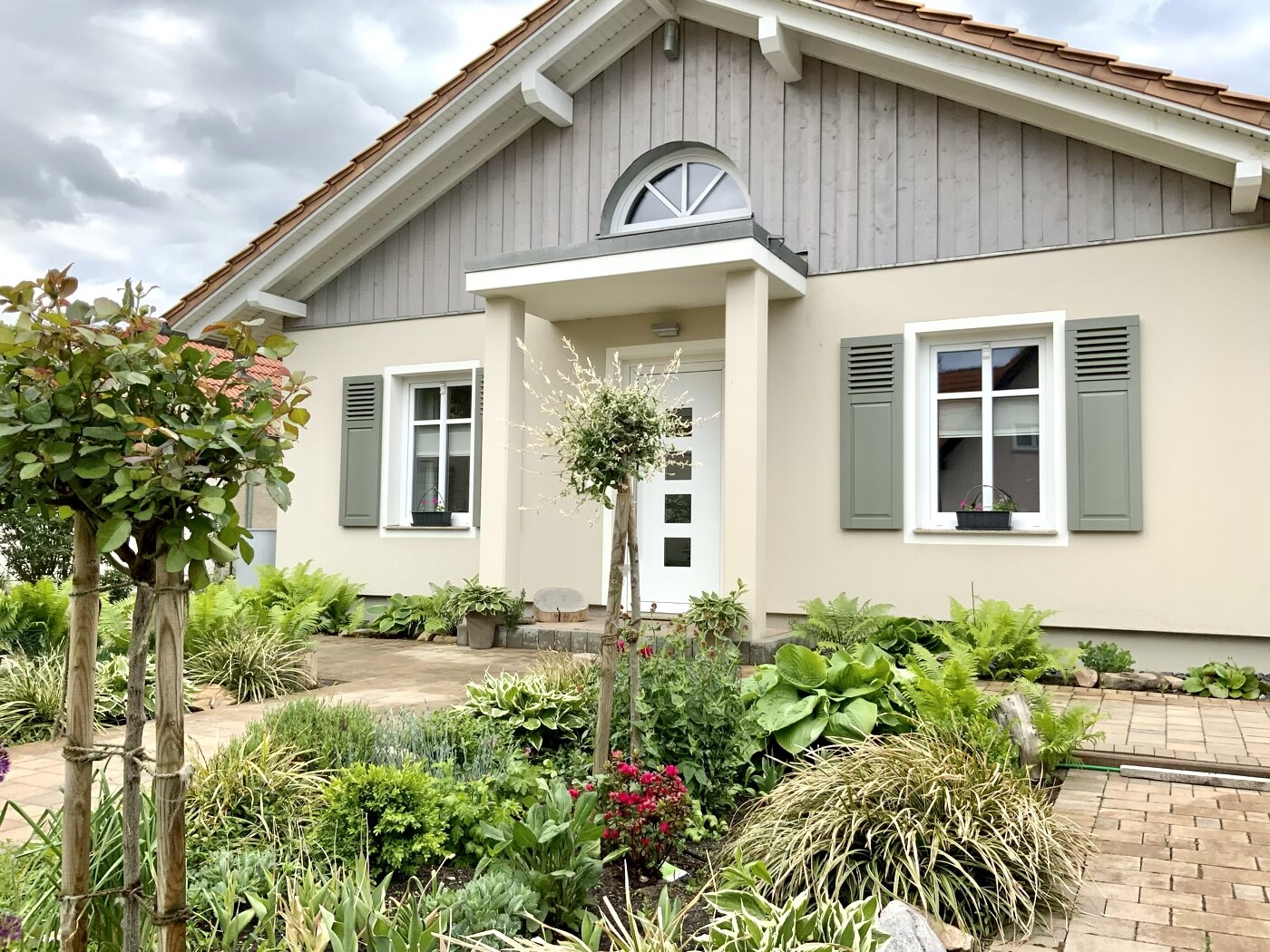 Front view of a detached house with gray shutters and garden.
