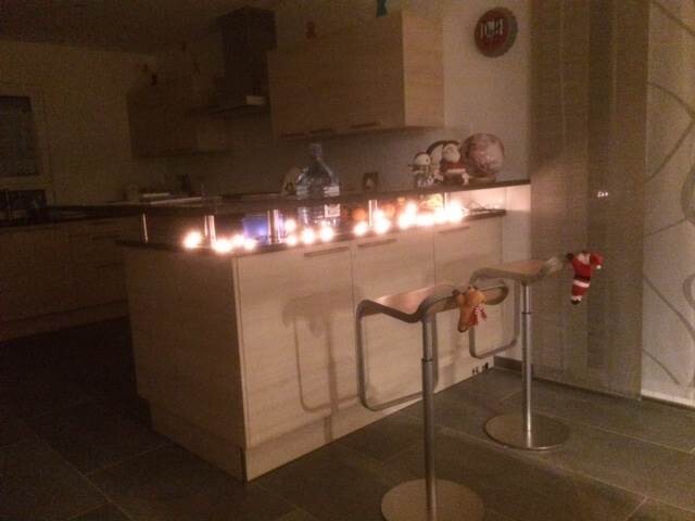 Modern kitchen with island, bar stools and Christmas decorations in warm lighting.