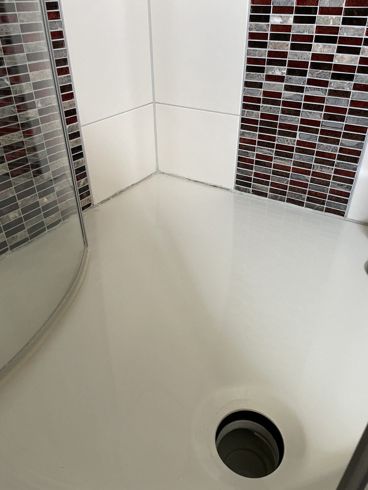 Shower in bathroom with white tiles, colorful mosaic wall, and round floor drain.