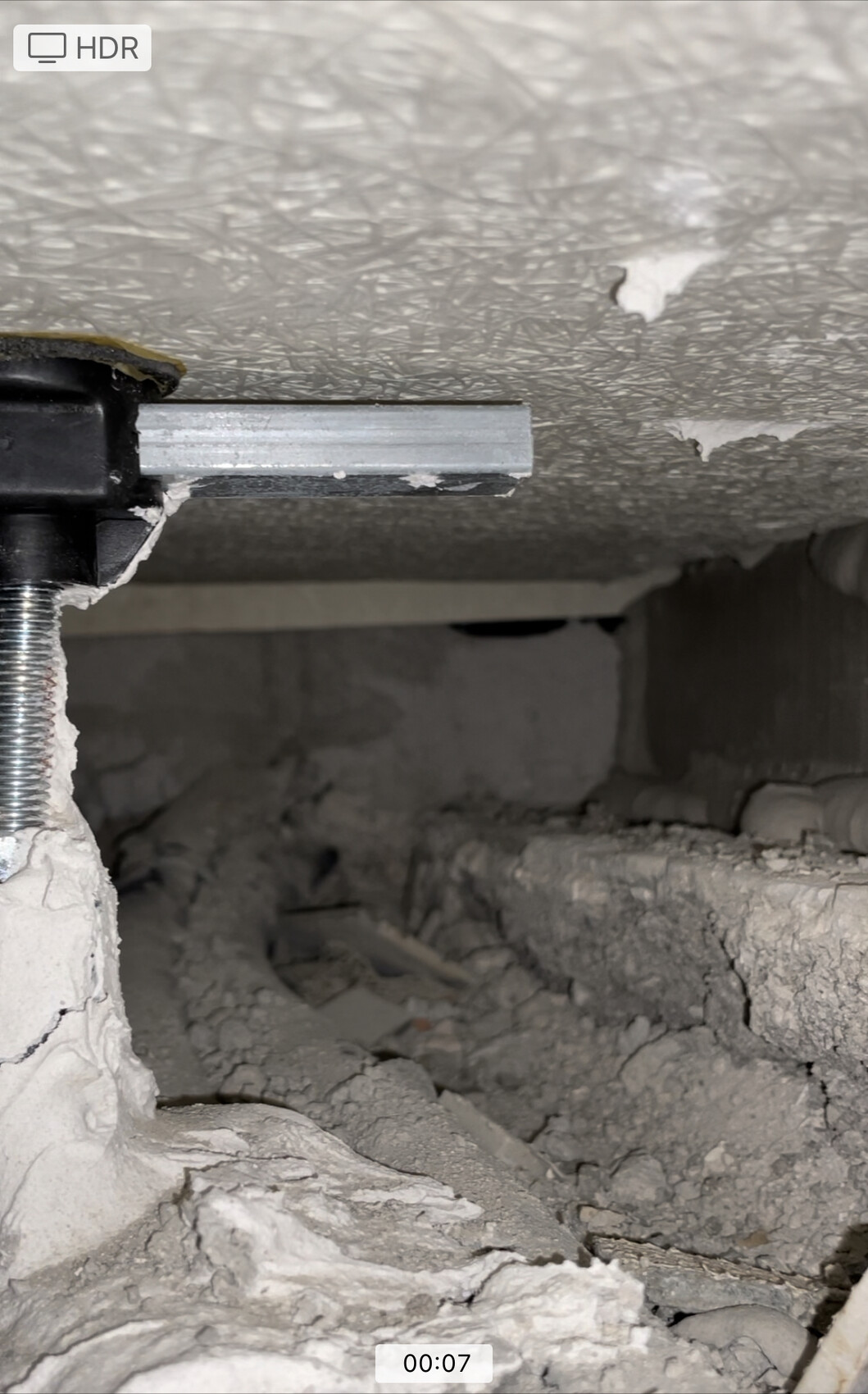 Shell construction scene with demolition debris, plaster rubble, and metal bracket in the wall.