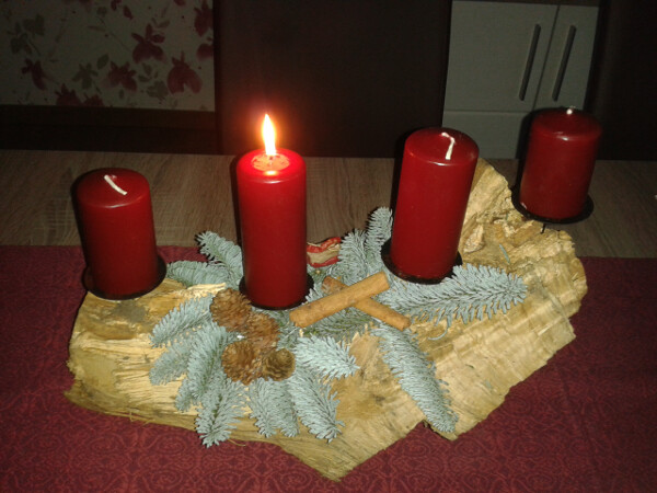 Adventskranz aus Holzscheibe mit vier roten Kerzen, Tannenzweigen, Zimtstangen.