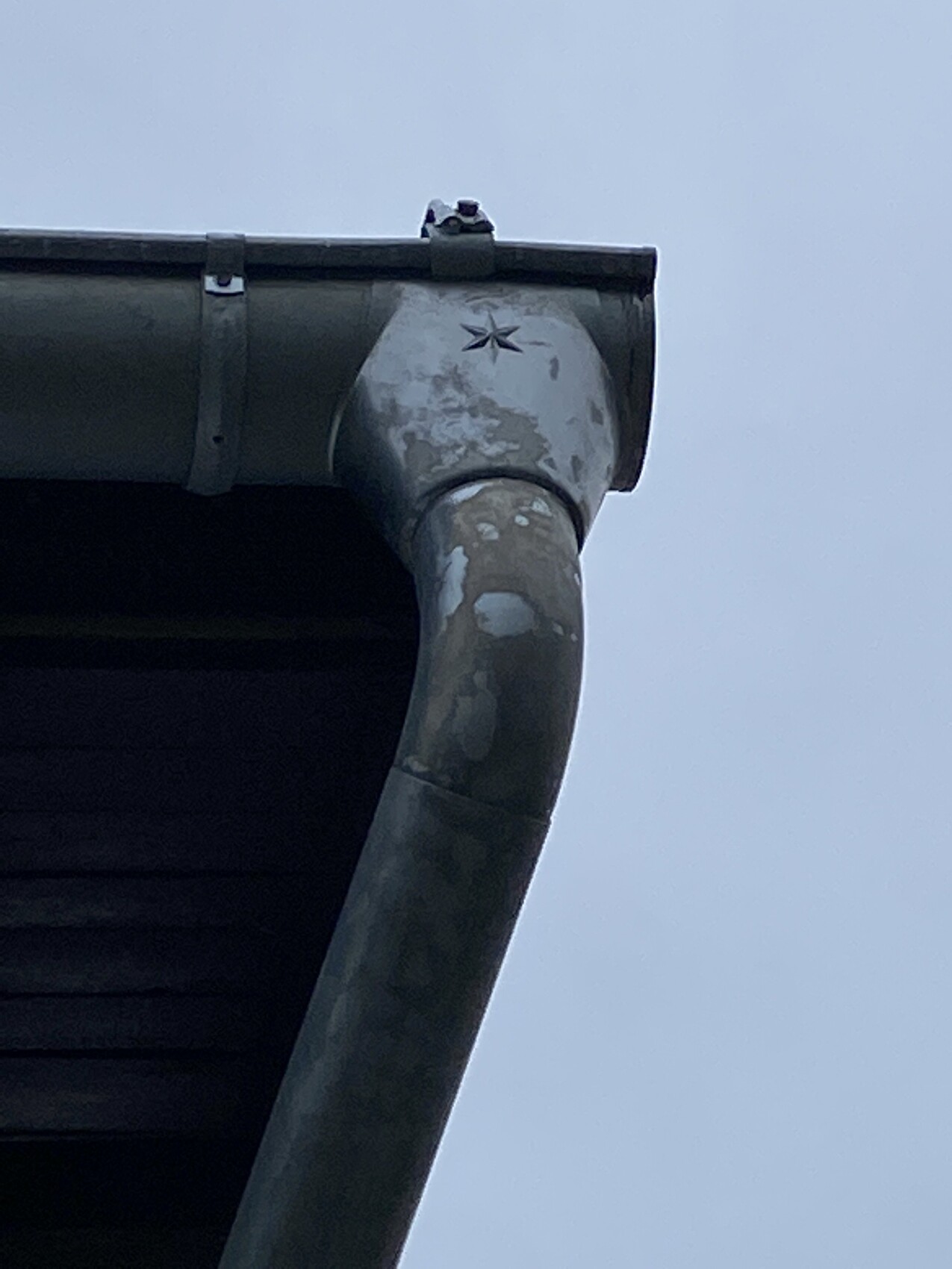 Close-up of a gutter with downspout at the roof edge, coating peeling off.