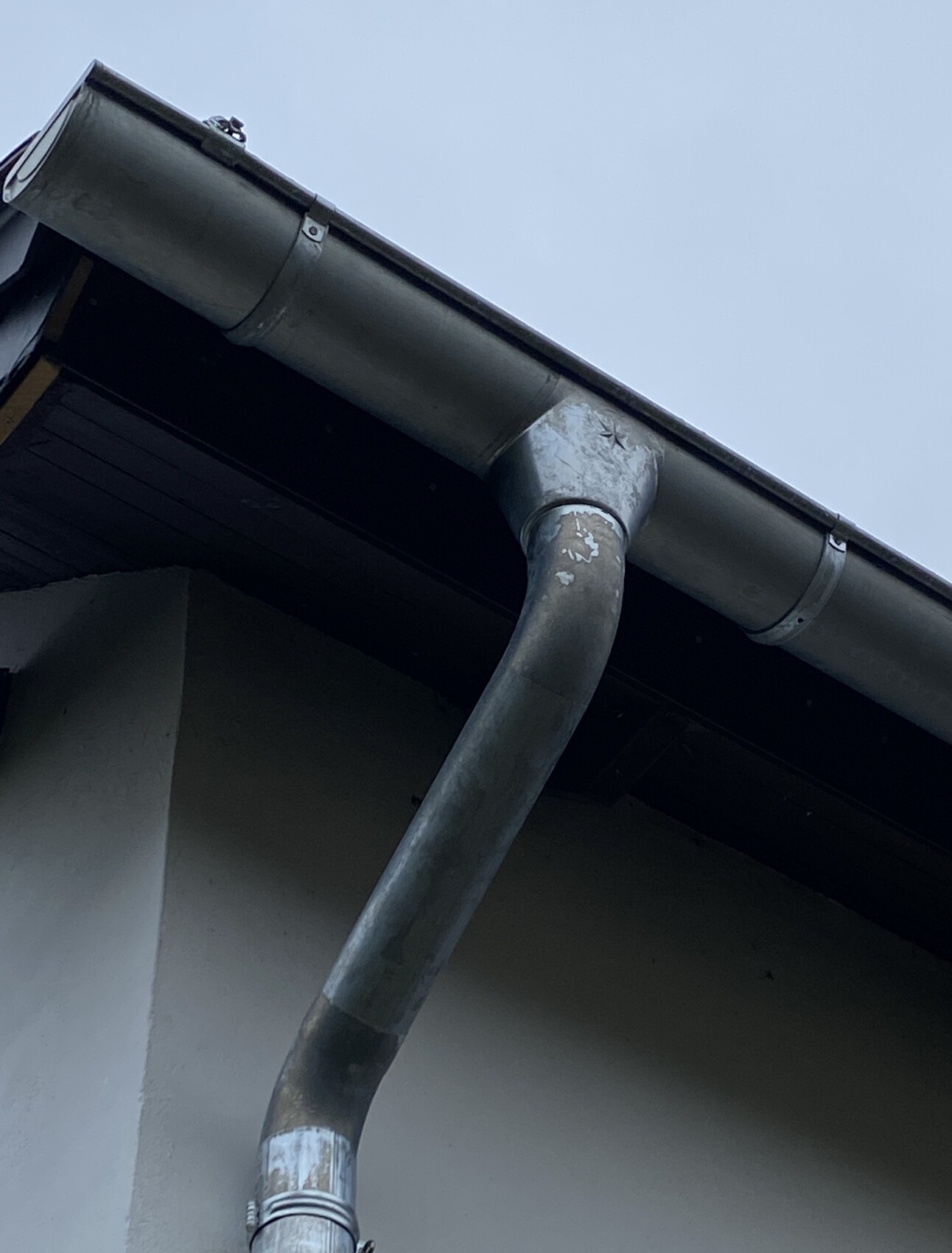 Close-up of a gray downspout leading from a rain gutter on the house, blue sky.